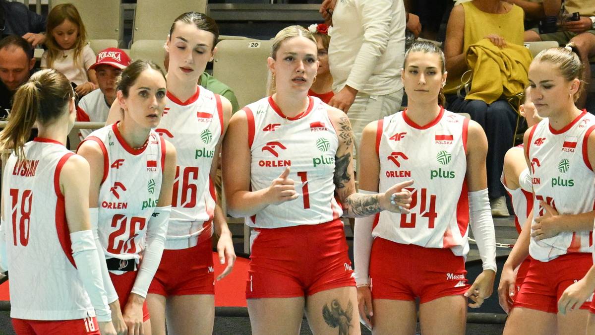 Grupa siatkarek reprezentacji Polski w białych strojach z czerwonymi detalami, stojące razem na boisku.