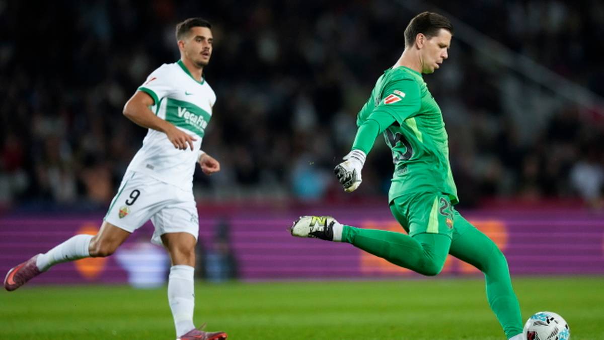 Piłkarz w białej koszulce biegnie po boisku, a bramkarz w zielonym stroju wykonuje kopnięcie piłki.