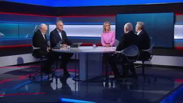 Cztery osoby siedzą przy okrągłym stole w studiu telewizyjnym. Dw&oacute;ch mężczyzn siedzi po jednej stronie stołu, a po drugiej stronie siedzą mężczyzna i kobieta.