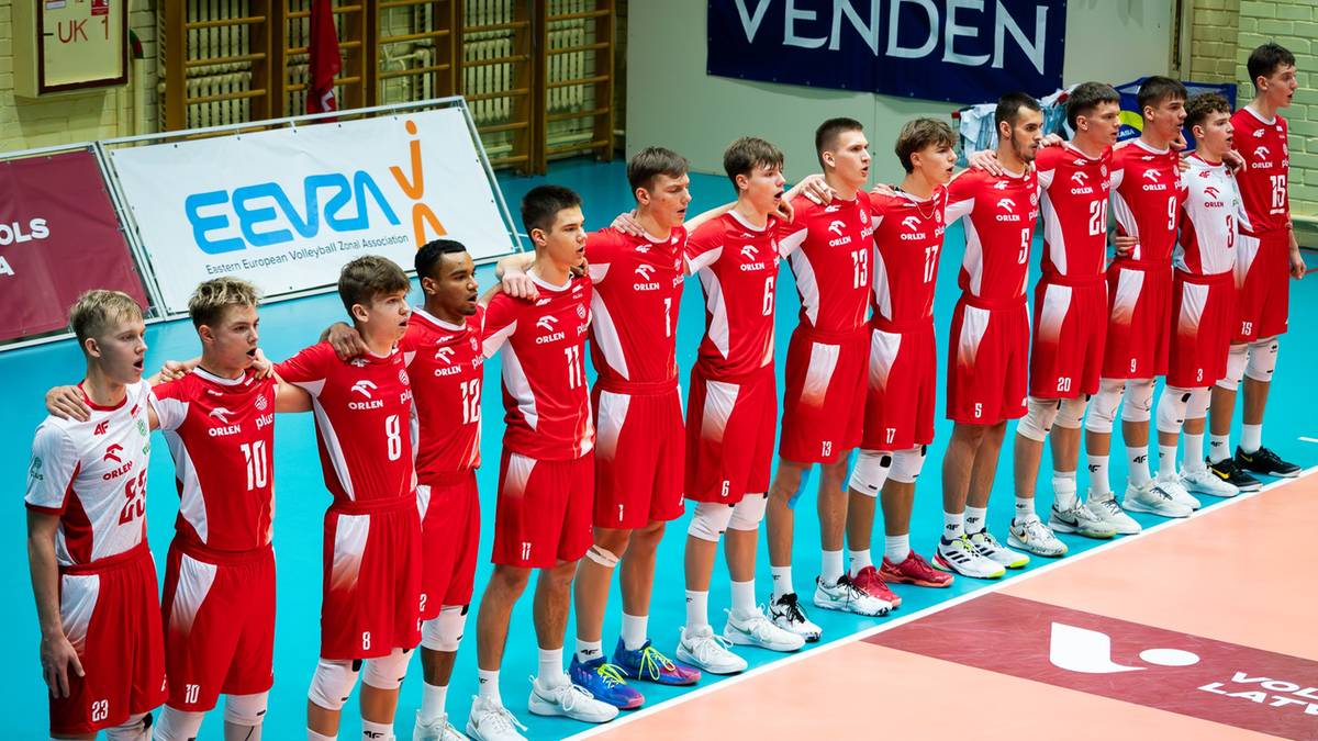 Drużyna siatkarzy w czerwonych strojach pozuje do zdjęcia, stojąc w rzędzie.