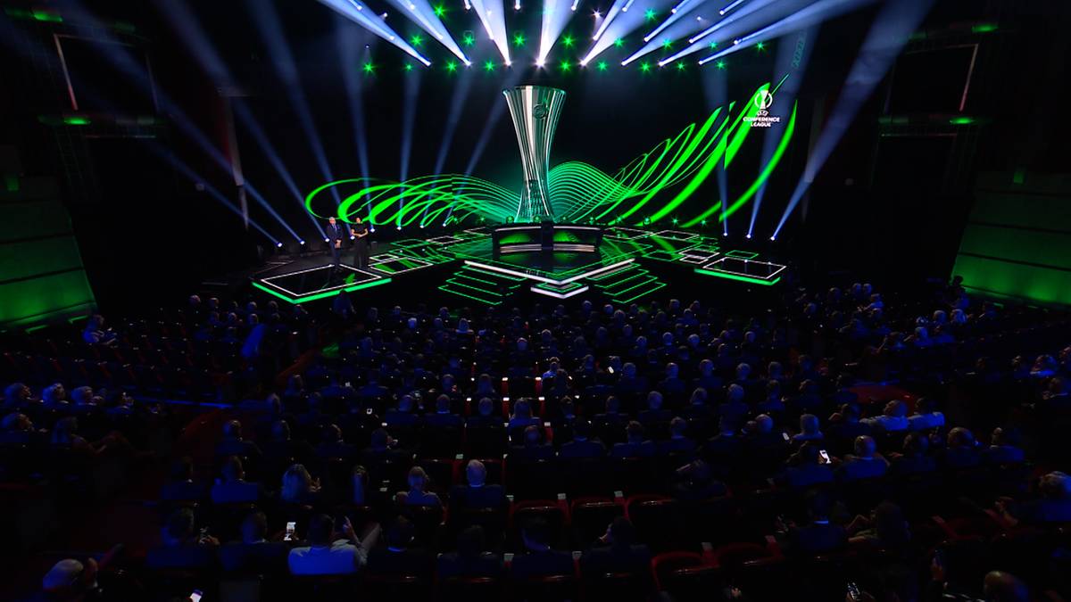 Scena z futurystyczną dekoracją w kształcie spirali i oświetleniem w kolorze zielonym i białym, gdzie prezentowane jest trofeum Ligi Konferencji. Widownia siedzi w ciemności.