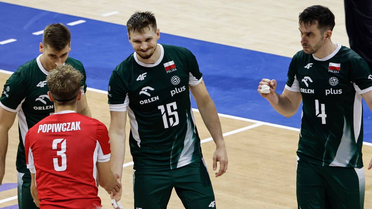 Siatkarze w zielonych strojach z numerami 15 i 4, oraz jeden w czerwonej koszulce z numerem 3, stoją na boisku i rozmawiają.