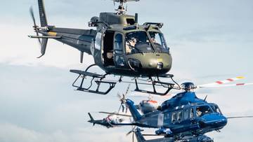 Dwa wojskowe helikoptery w locie, jeden ciemnozielony, drugi niebieski.