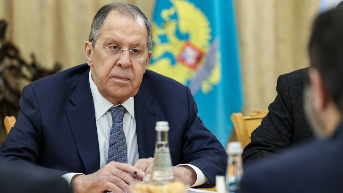 Siergiej Ławrow siedzi przy stole w garniturze i krawacie, z butelką wody przed sobą. Za nim widoczna jest flaga Rosji.