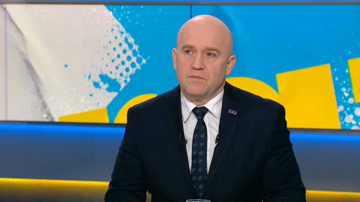 Mężczyzna w garniturze siedzi przed ekranem z niebiesko-ż&oacute;łtym wzorem.