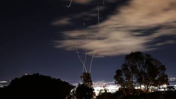 Niebo nocą z widocznymi smugami rakiet lub dron&oacute;w przecinającymi chmury.