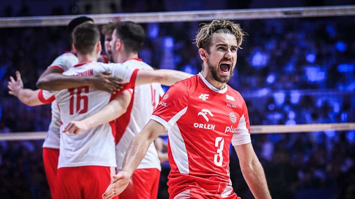 Siatkarz w czerwonej koszulce z numerem 3 krzyczy z radości, obejmując kolegów z drużyny w białych koszulkach.