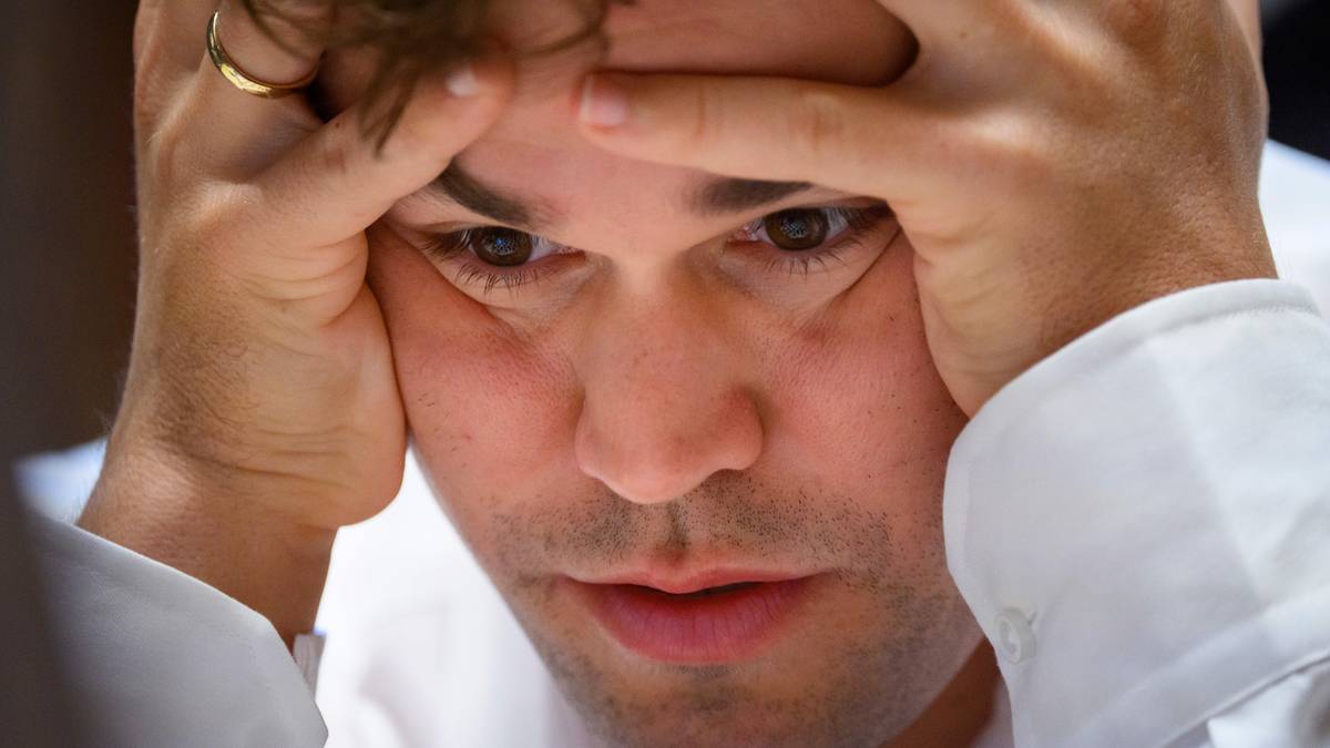 Zbliżenie na twarz szachisty Magnusa Carlsena, który trzyma ręce na czole, z widocznym skupieniem i zaniepokojeniem.