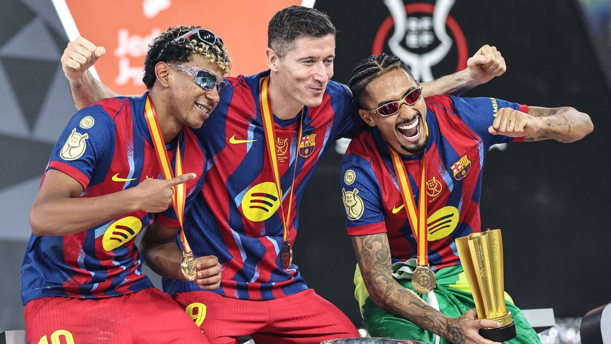 Trzech piłkarzy w strojach FC Barcelony świętuje zwycięstwo, jeden z nich trzyma trofeum.