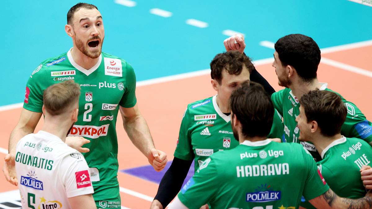 Grupa siatkarzy w zielonych strojach sportowych, jeden z nich krzyczy z radości, otoczony przez koleg&oacute;w z drużyny na boisku.