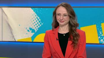 Kobieta w okularach i czerwonym żakiecie uśmiecha się, na tle ekranu z grafiką.