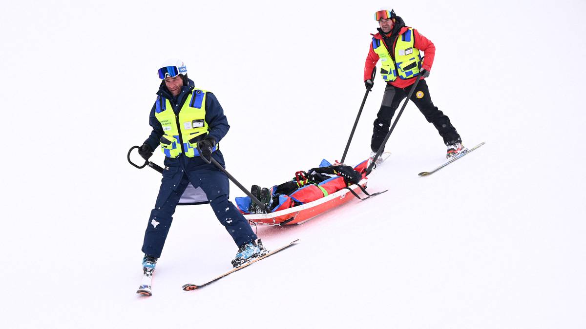 Dwóch ratowników narciarskich na nartach transportuje osobę na noszach po zaśnieżonym stoku.