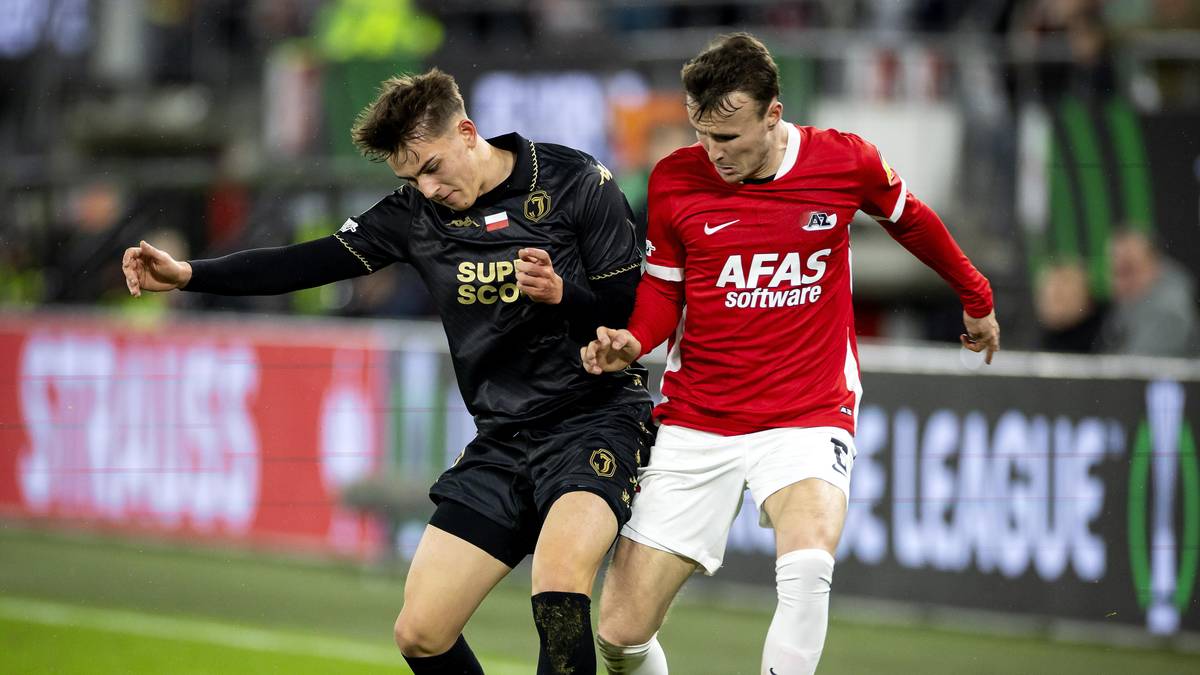 Dwóch piłkarzy walczących o piłkę na boisku podczas meczu.