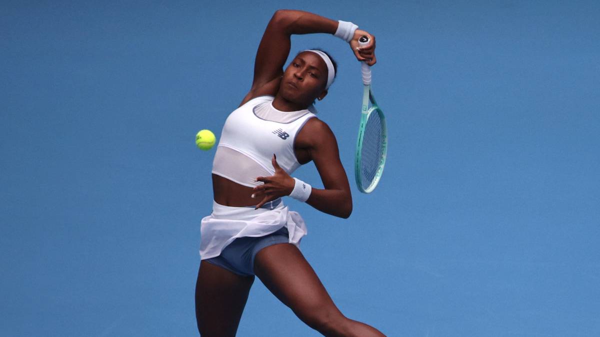 Amerykańska tenisistka Coco Gauff podczas uderzenia serwisowego na tle niebieskiego tła.