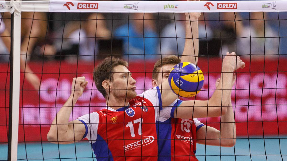 Dwóch siatkarzy rywalizuje przy siatce, jeden z nich próbuje zablokować piłkę uderzoną przez przeciwnika.