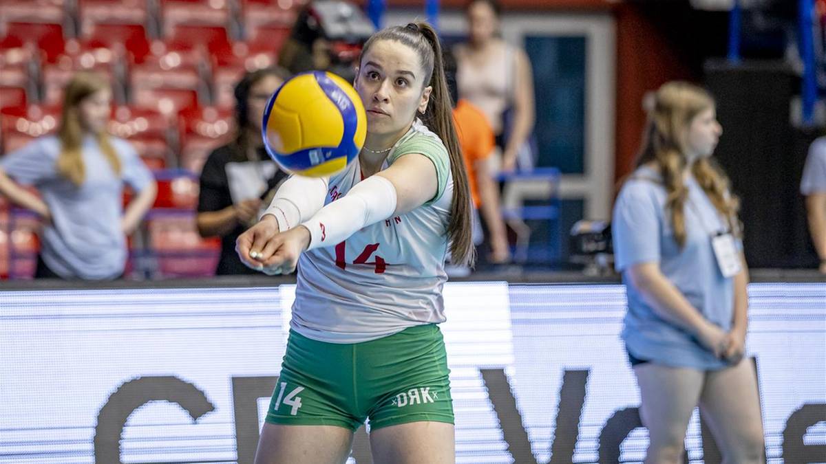 Siatkarka w zielonych spodenkach i szarej koszulce z numerem 14 na przedramieniu odbija piłkę do siatk&oacute;wki.