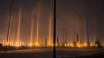 Słupy świetlne o pomarańczowej barwie unoszące się nad nocnym miastem.