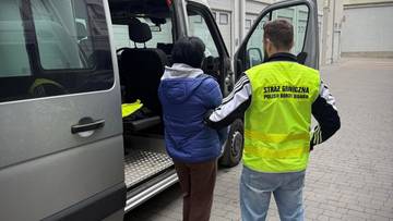 Dw&oacute;ch mężczyzn, jeden w kamizelce odblaskowej Straży Miejskiej, stoi obok otwartych drzwi białego vana.