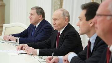 Prezydent Rosji Władimir Putin siedzi przy stole z innymi mężczyznami podczas spotkania.