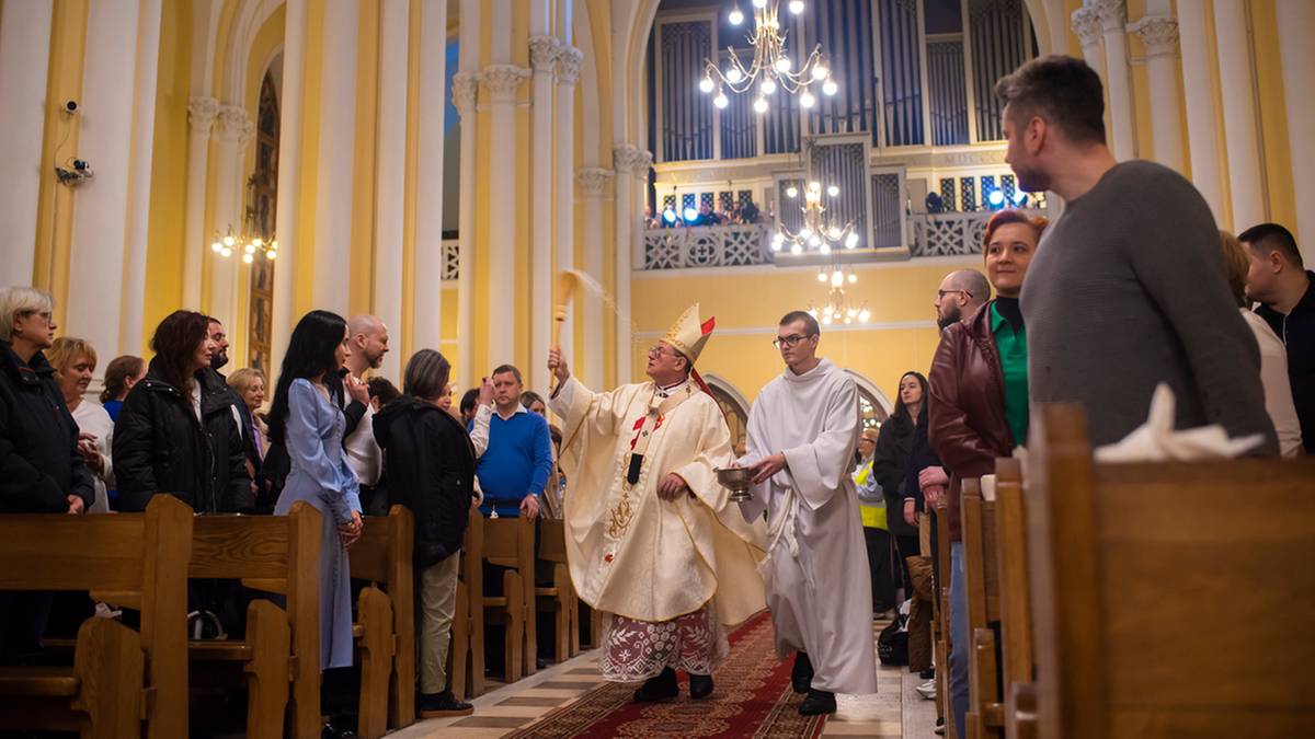 Biskup w szatach liturgicznych błogosławi wiernych zgromadzonych w kościele podczas mszy rezurekcyjnej.