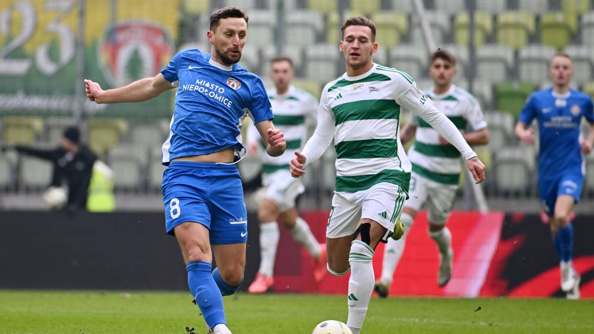 Dwóch piłkarzy w akcji, jeden w niebieskiej koszulce i krótkich spodenkach z numerem 8, drugi w zielono-białej koszulce w paski. Obaj biegają po boisku.