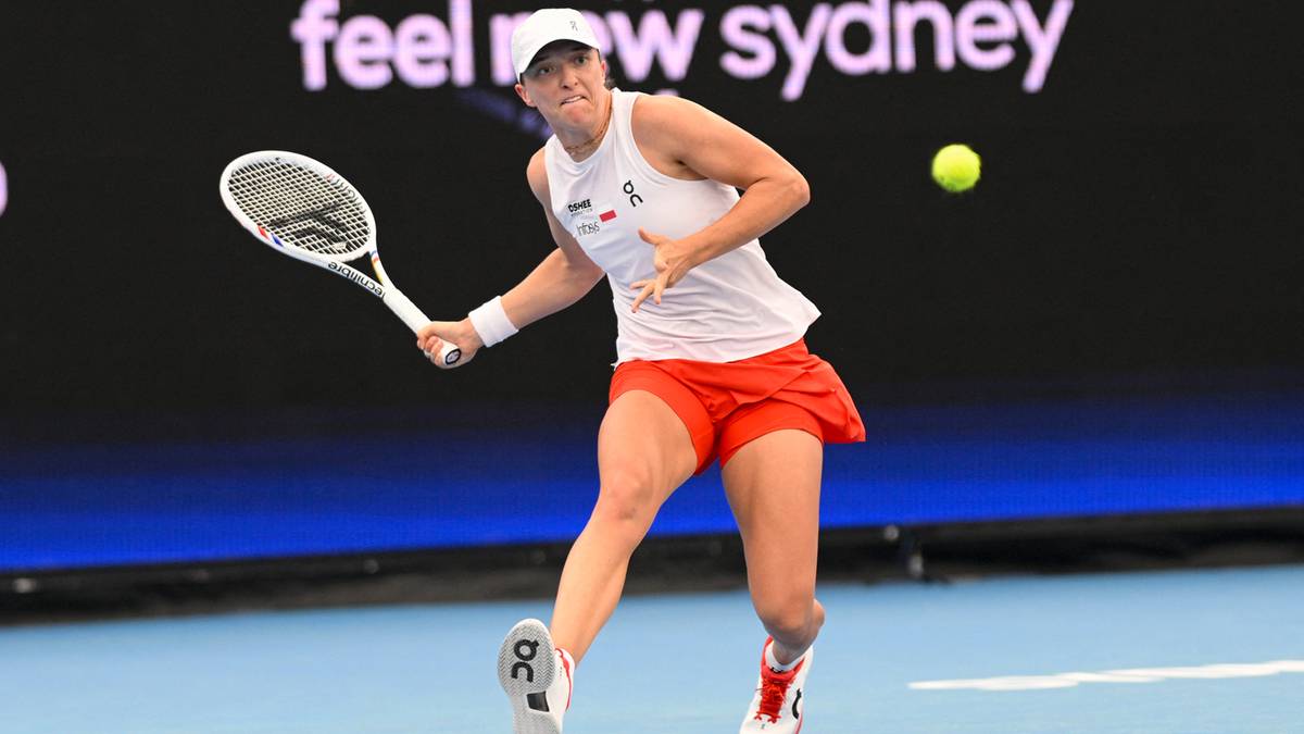 Tenisistka w białej koszulce i pomarańczowej sp&oacute;dniczce odbija piłkę rakietą na korcie tenisowym.