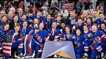 Drużyna hokejowa kobiet USA z medalem olimpijskim w otoczeniu kibic&oacute;w i sztabu trenerskiego.