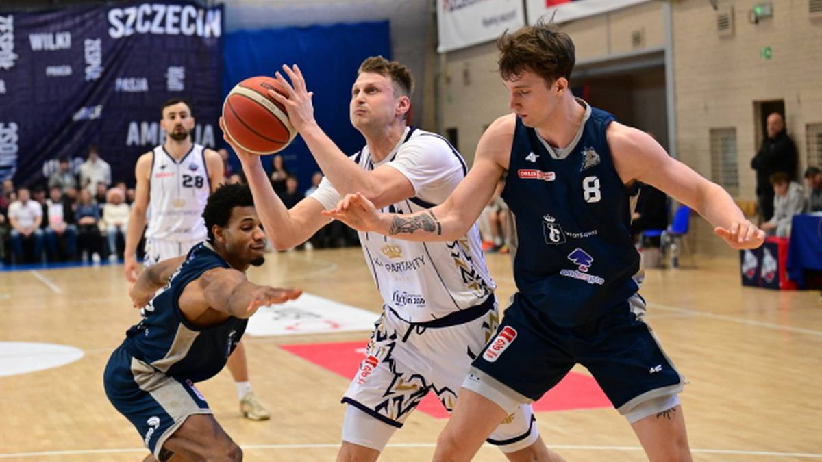 Trzech zawodników koszykówki walczy o piłkę podczas meczu, jeden z nich próbuje wykonać rzut.