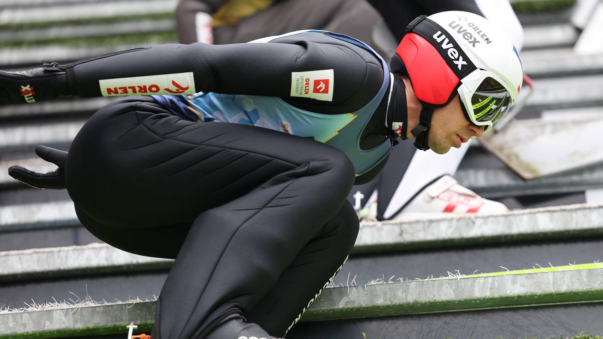 Skoczek narciarski w pozycji startowej, przygotowujący się do zjazdu.