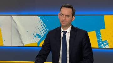 Mężczyzna w garniturze siedzi w studiu telewizyjnym.