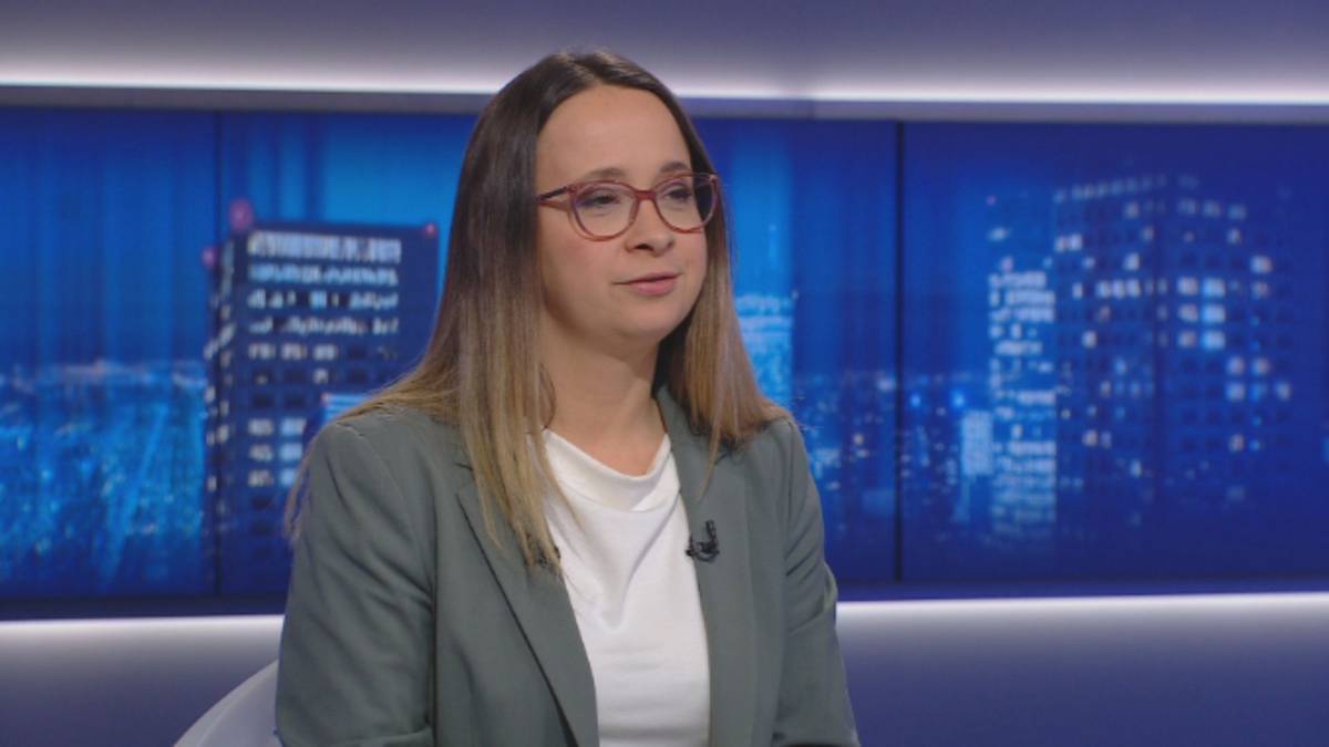 Kobieta w okularach i marynarce siedzi w studiu telewizyjnym.