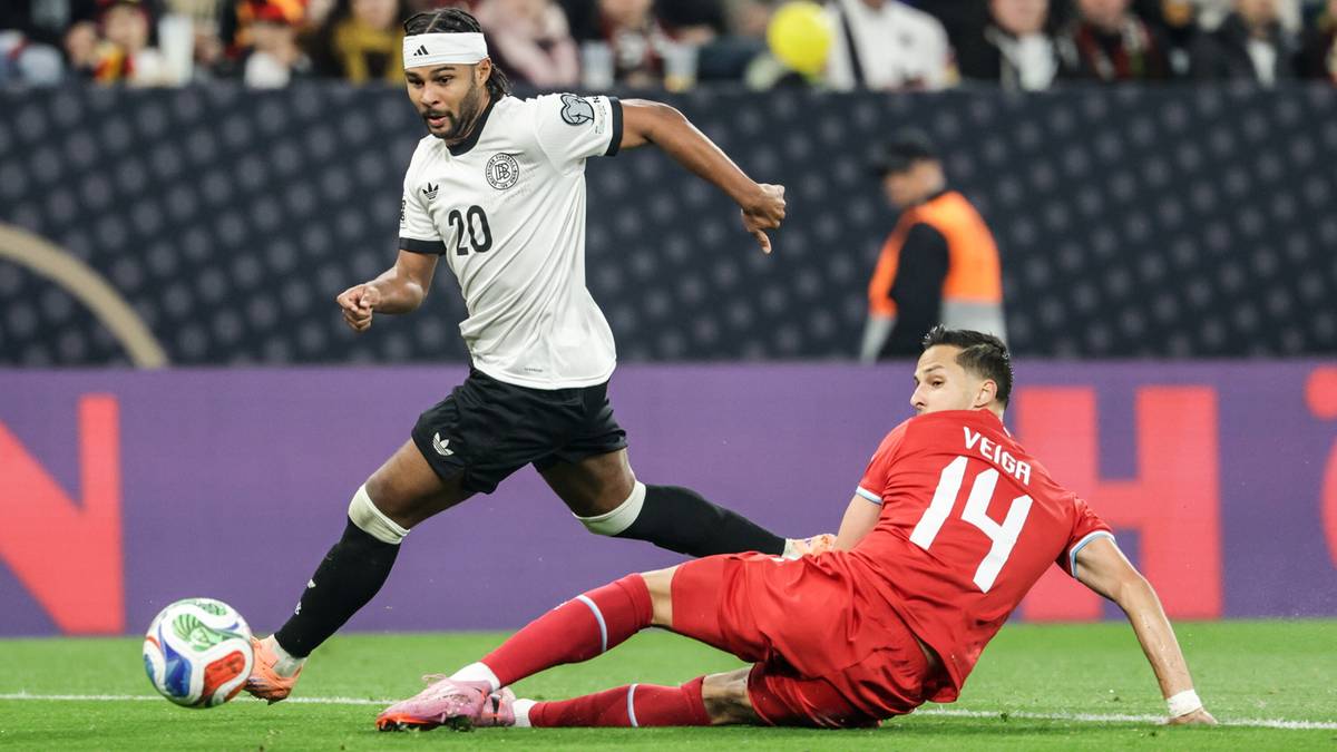 Piłkarz w białej koszulce z numerem 20 i opaską na głowie biegnie z piłką. Gracz w czerwonej koszulce z numerem 14 leży na trawie obok niego.