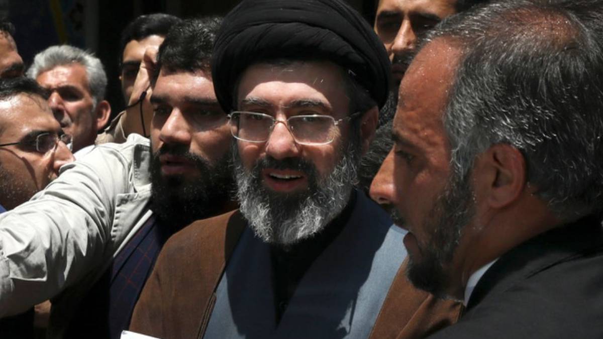 Portret duchownego w czarnym turbanie i okularach, otoczonego przez innych mężczyzn.