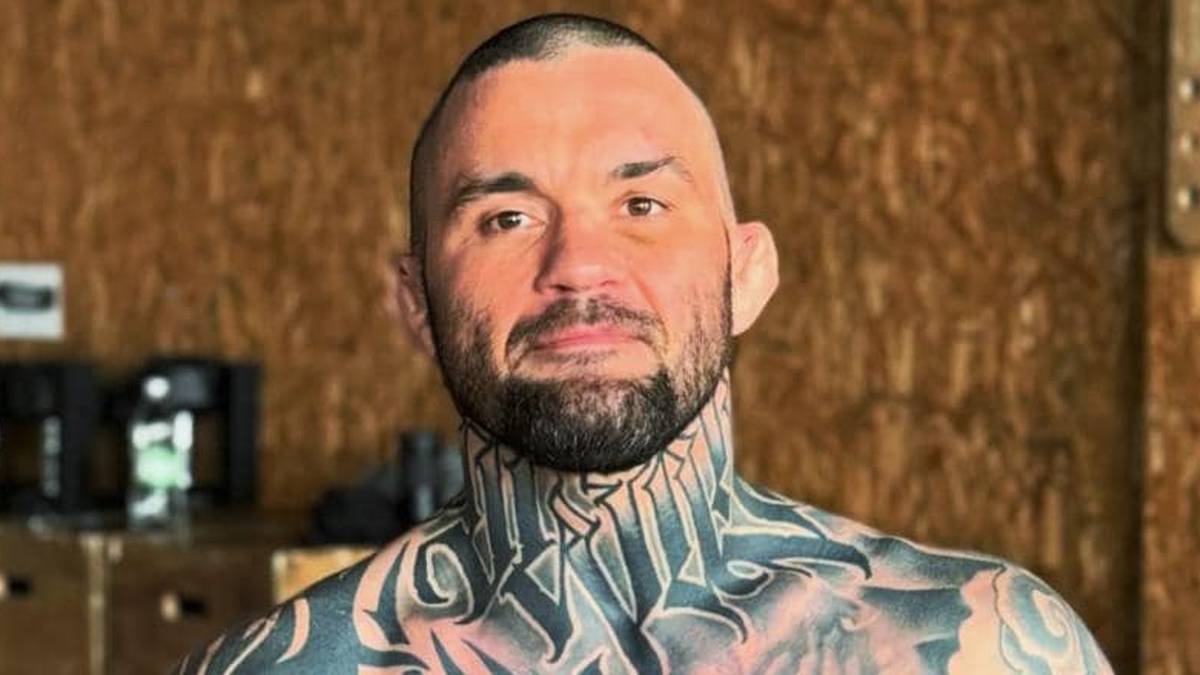 Dwóch mężczyzn, zawodników MMA, pozuje do zdjęcia w sali treningowej. Jeden z nich ma widoczne tatuaże na klatce piersiowej i ramionach.