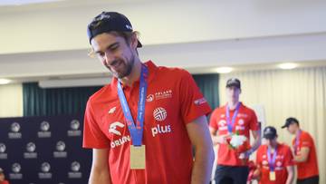 Siatkarz Jakub Popiwczak w czerwonej koszulce z medalem na szyi i bukietem kwiat&oacute;w w ręku podczas powitania reprezentacji Polski po wygraniu Ligi Narod&oacute;w.