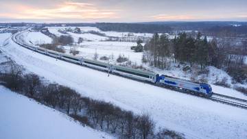 Pociąg PKP Intercity poruszający się po zaśnieżonej linii kolejowej zimą.