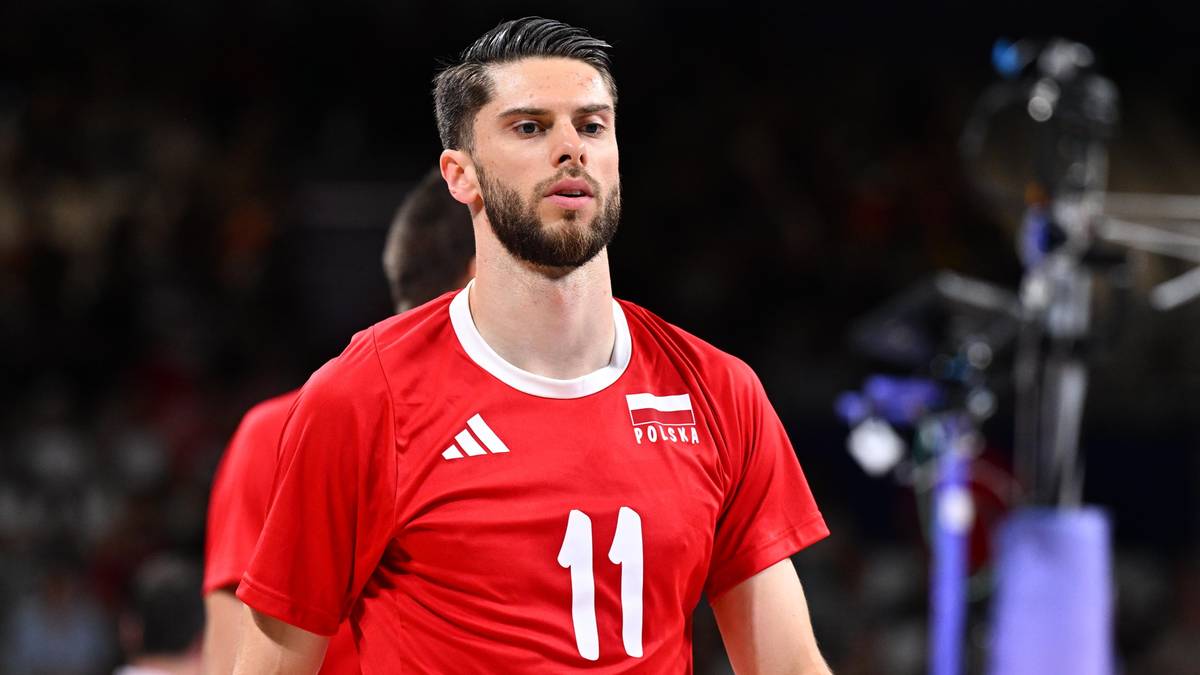 Mężczyzna w czerwonej koszulce siatkarskiej z numerem 11, ubrany w biały kołnierzyk, z krótkimi, ciemnymi włosami i brodą.