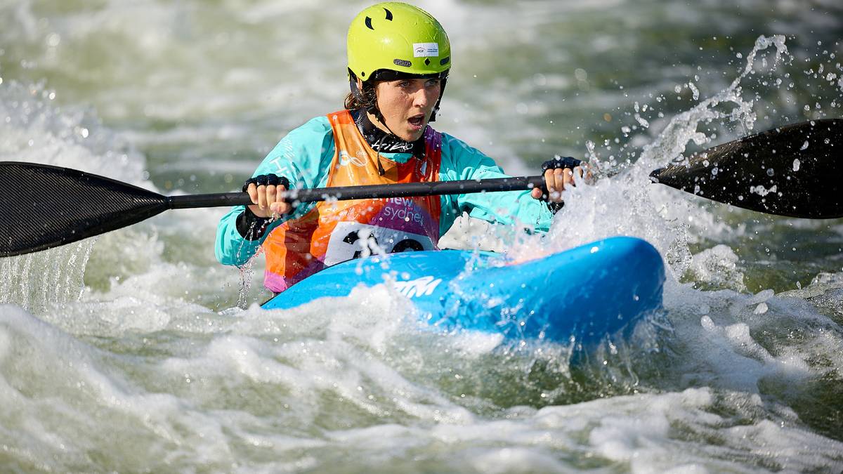 Kobieta w kasku i kamizelce ratunkowej wiosłuje w niebieskim kajaku po rwącej rzece.