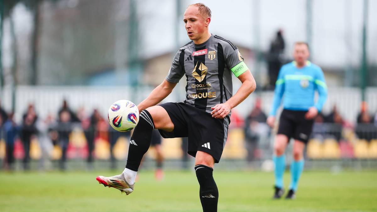 Piłkarz w szaro-czarnym stroju prowadzi piłkę nogą na boisku.