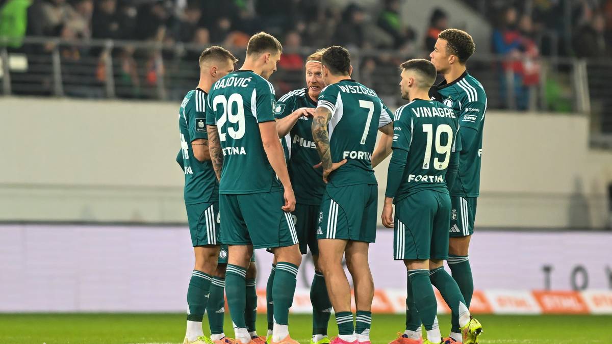 Drużyna piłkarska w zielonych strojach zgromadzona w kółku na boisku.