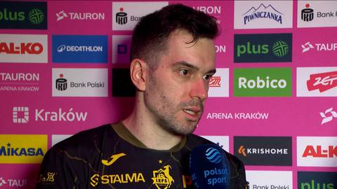 Marcin Komenda, siatkarz, udzielający wywiadu na tle r&oacute;żowej ścianki z logotypami sponsor&oacute;w.