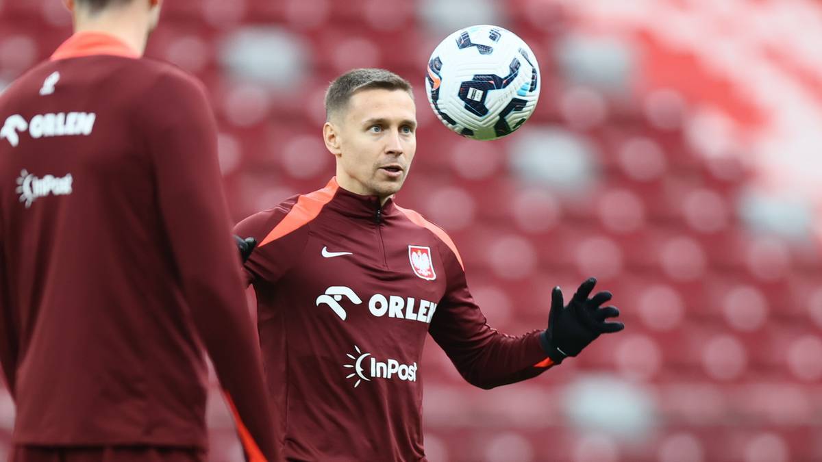 Piłkarz reprezentacji Polski w bordowej koszulce z biało-czerwonym orłem trenuje z piłką na boisku.