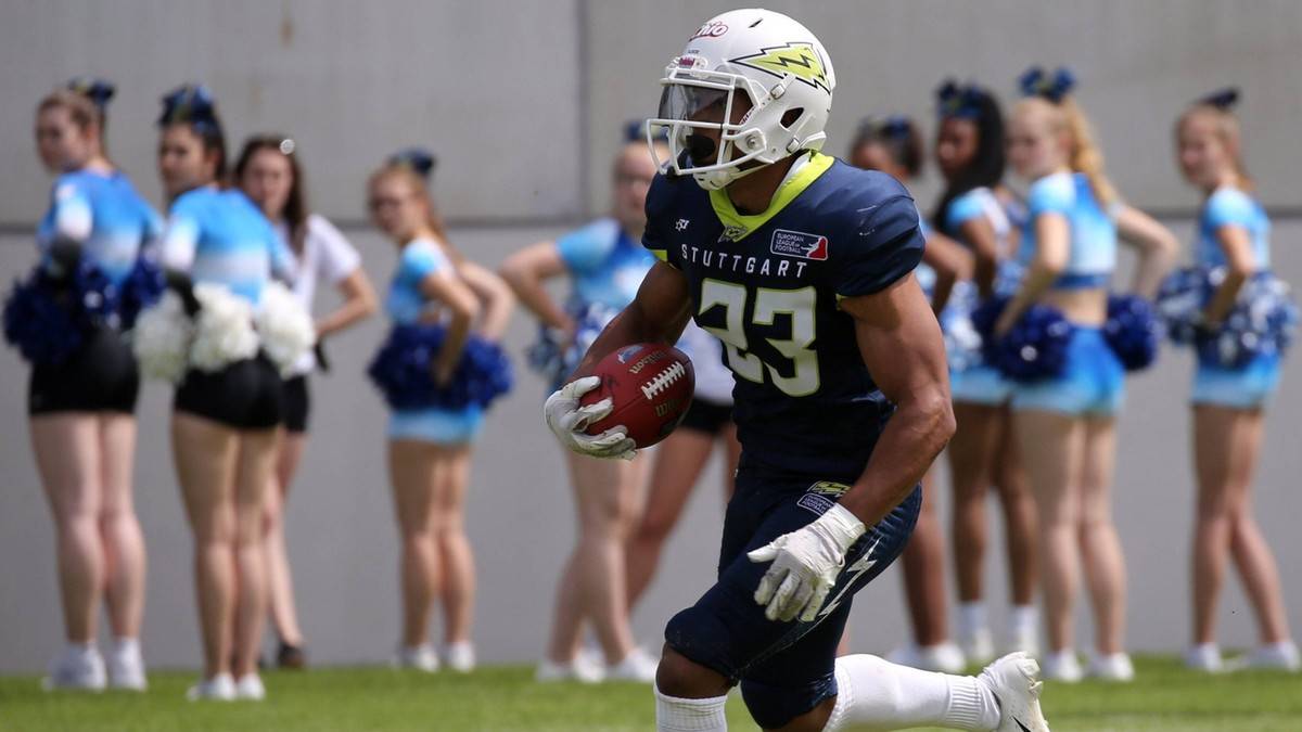 Gracz drużyny Stuttgart Surge w niebieskim stroju z numerem 33 biegnie z piłką do futbolu amerykańskiego. W tle widać cheerleaderki w niebieskich strojach z pomponami.