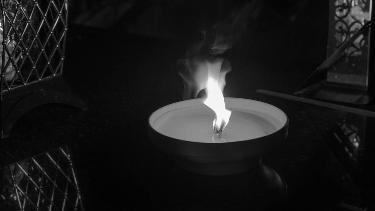 Płomień świecy w ciemnym otoczeniu, oświetlający fragmenty ozdobnych lampionów.