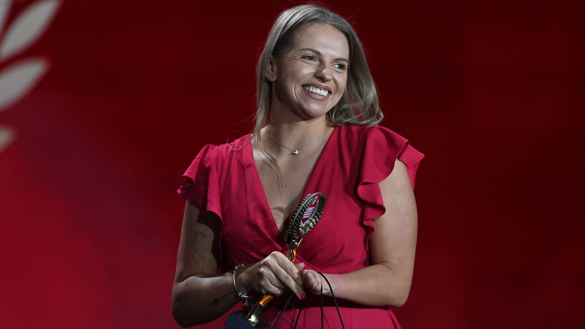 Kobieta w czerwonej sukience z falbankami trzyma nagrodę w ręku, uśmiecha się.