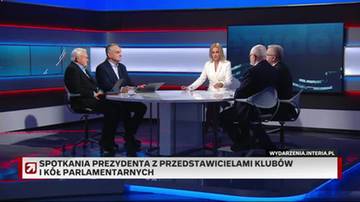 Cztery osoby siedzą przy okrągłym stole w studiu telewizyjnym. Jedna kobieta w białej marynarce rozmawia z trzema mężczyznami. W tle znajduje się duży ekran z widokiem nocnego miasta.