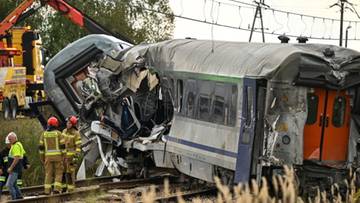 Zdjęcie przedstawia ciężki wypadek kolejowy z wykolejonymi i zniszczonymi wagonami, obok kt&oacute;rych stoją ratownicy.