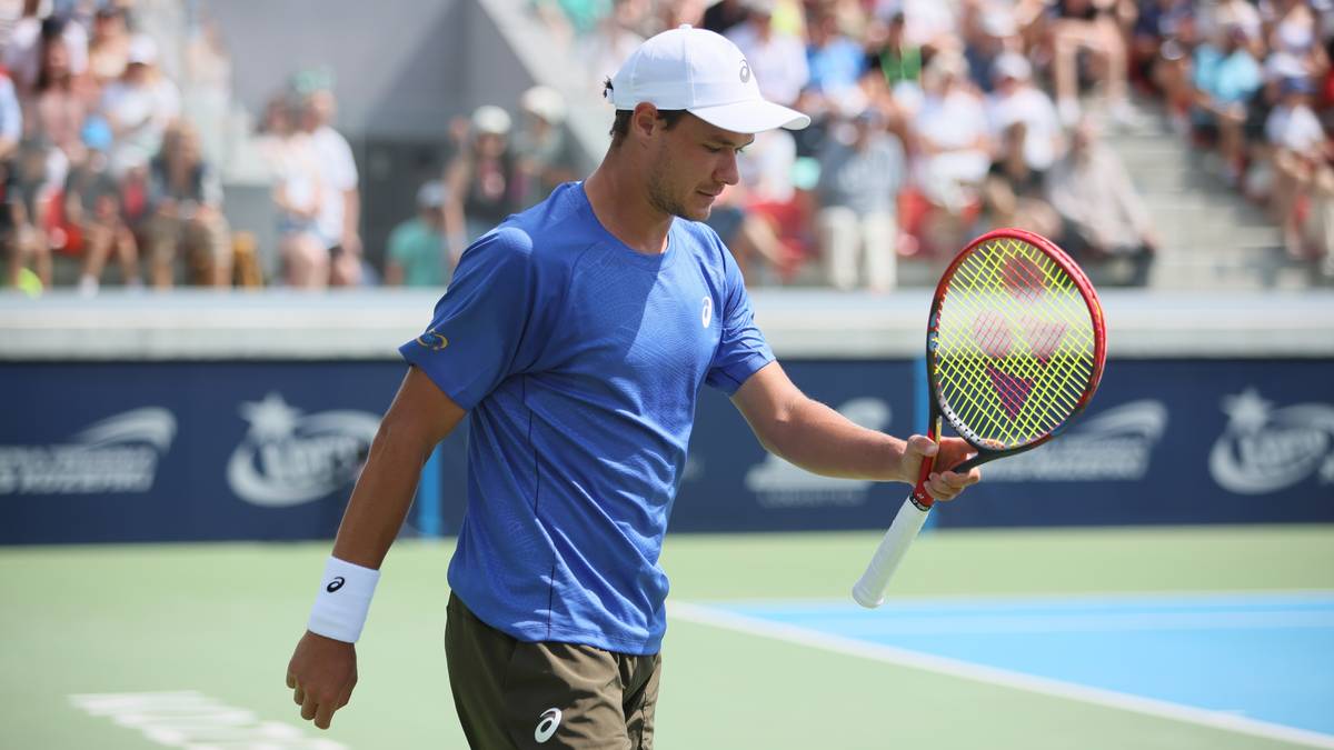 Tenisista Kamil Majchrzak w białej czapce i niebieskiej koszulce, z rakietą w ręku, podczas meczu.