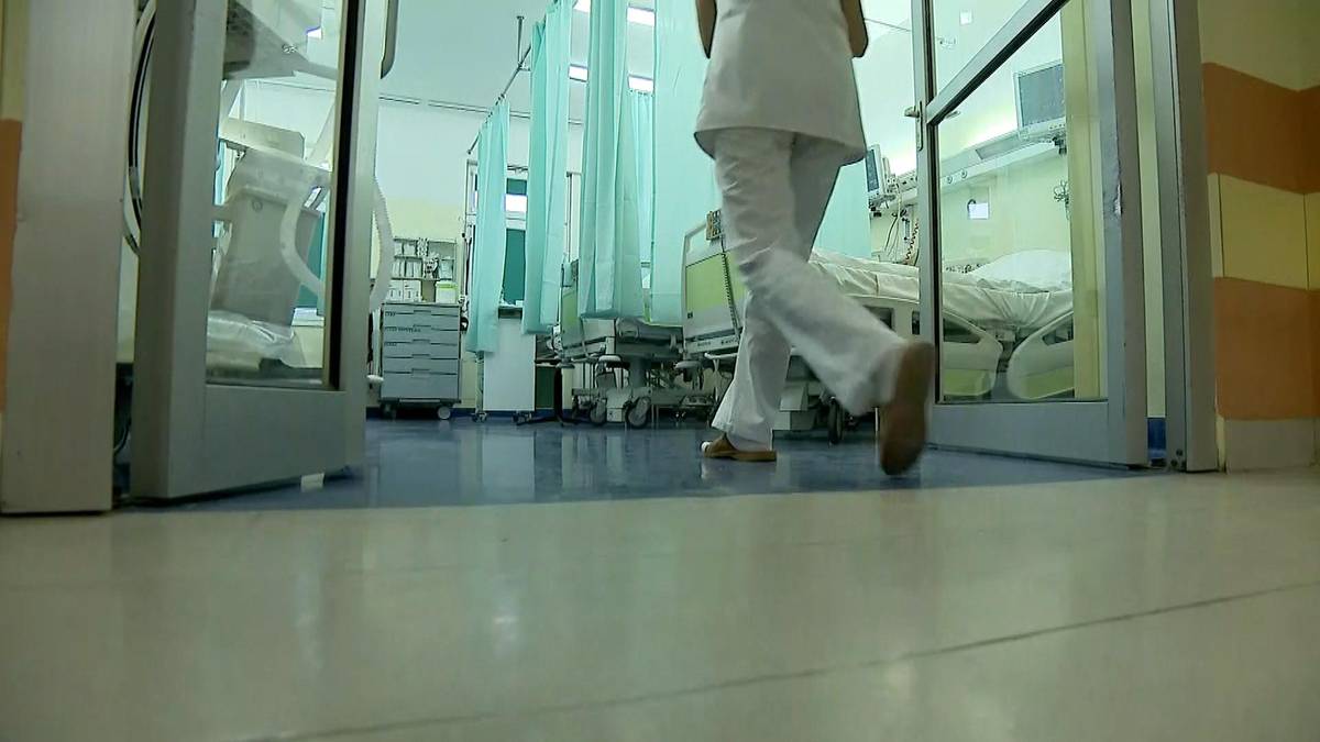 Osoba w białym stroju medycznym wchodzi do sali szpitalnej.