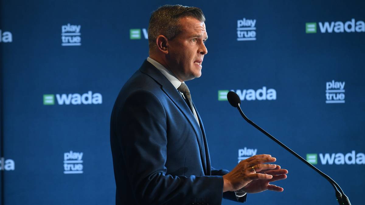 Portret Witolda Bańki, mówiącego do mikrofonu na tle z logo WADA.